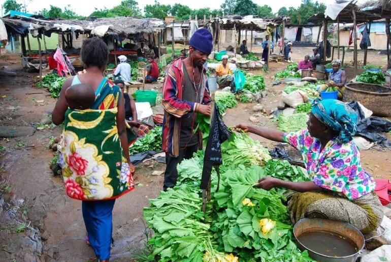 A market trader selling vegetables to a customer at an open air market
